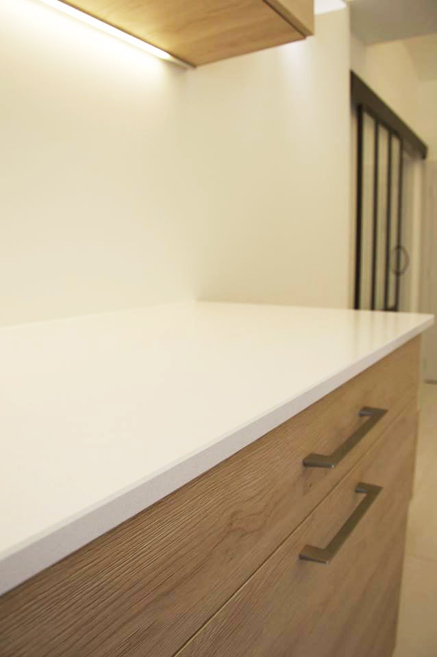 Façade et corps de meuble — Décors chêne Galdstone.
Poignées — Inox brossé.
Plan de travail — Quartz décors blanc pailleté.