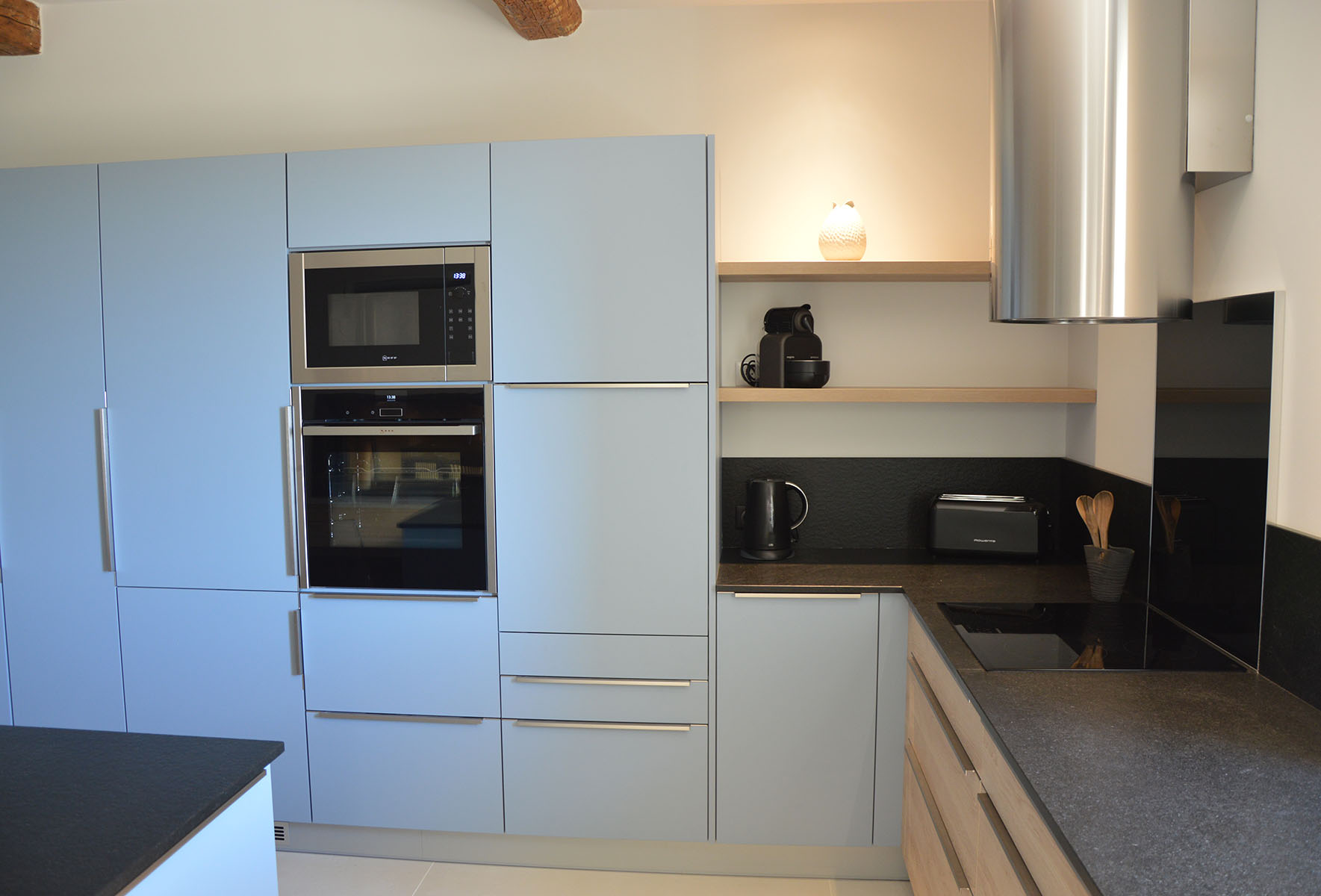 Façades — Décors bleu denim, chêne gladstone.
Poignées profil — Inox brossé.
Plan de travail et crédence — Granit noir.
Electroménager — Frigo, Four, micro-ondes, lave-vaisselle, plaque de cuisson, hotte.
Crédence de cuisson — Verre trempé noir.