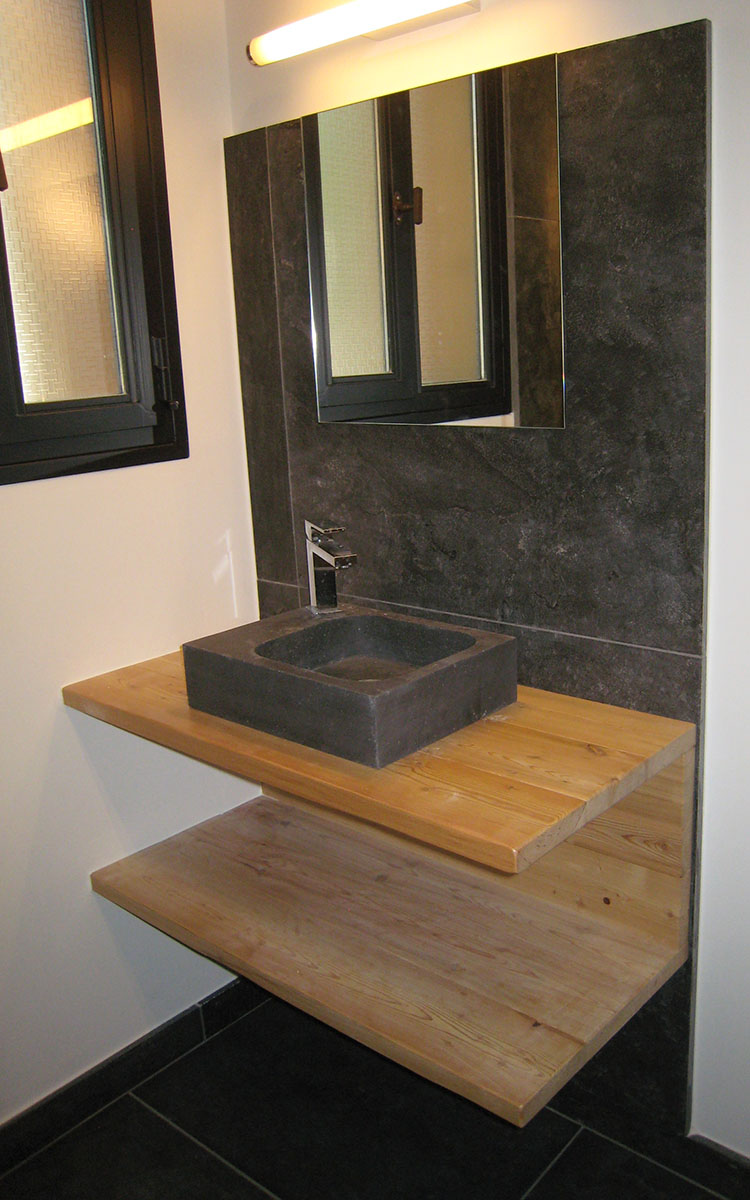 Meuble sous vasque — Mélèze de pays verni.
Vasque à poser — Pierre.
Equipement — Miroir, luminaire, robinet chromé.