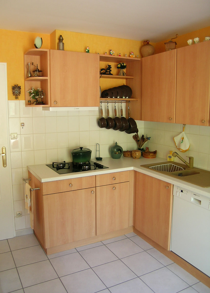 Façades — Décor hêtre.
Poignées — Bouton satiné.
Plan de travail —Décor blanc moucheté.
Évier encastré — Résine.
Electroménager — Plaque de cuisson, hotte, lave-vaisselle, frigo.