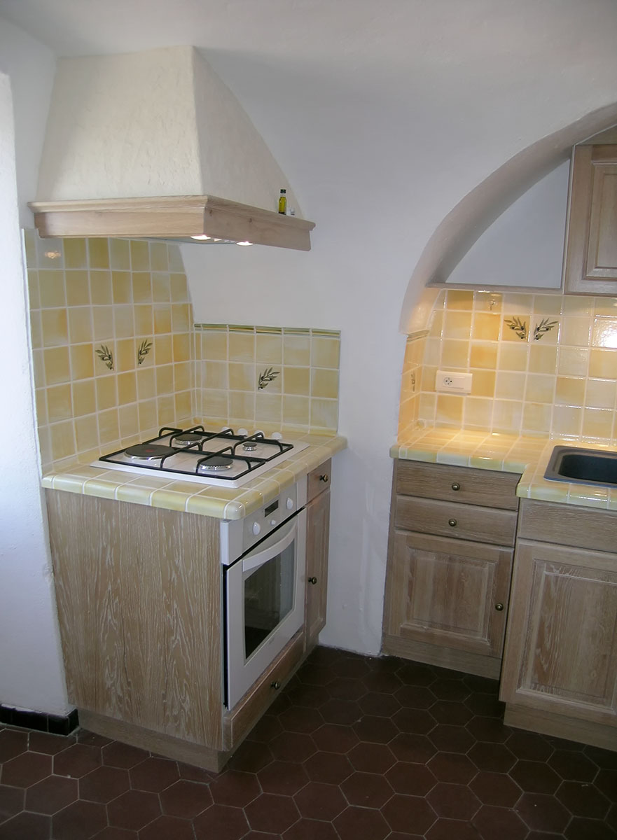 Façade — Chêne cérusé blanc, verni.
Plan de travail — Carrelage provençale.
Evier encastré — Résine.
Electroménager — Plaque de cuisson, hotte, four.