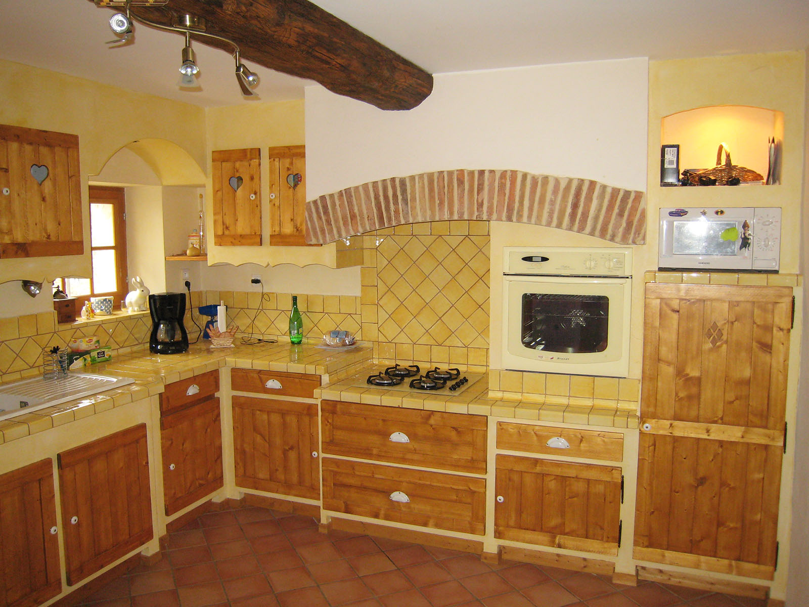 Façade — Epicéa, teinté vernis.
Poignées — Bouton céramique.
Plan de travail et crédence — Carrelage provencale.
Evier — Céramique
Electroménager — Four, micro-onde, plaque de cuisson, hotte.