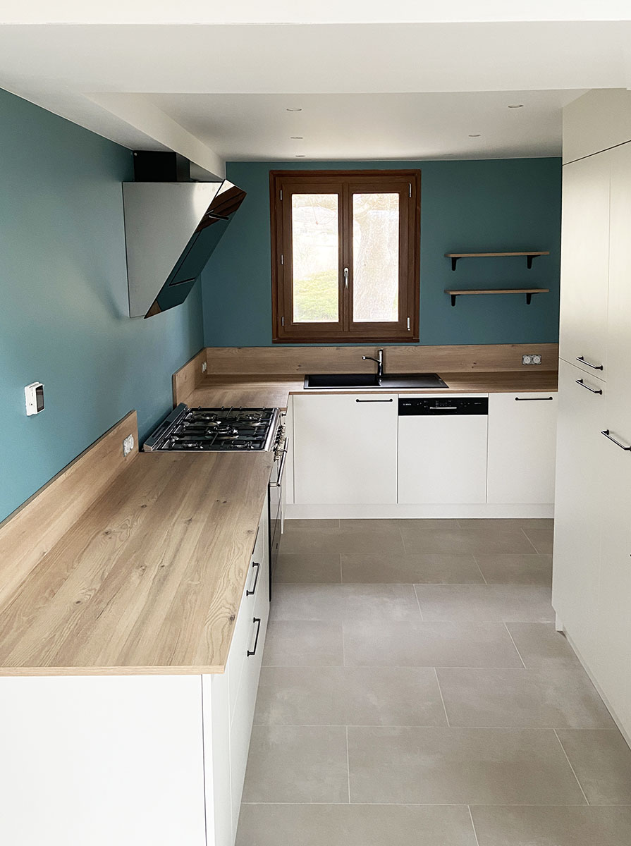 Meubles et Façades — Décor Orgeat Polyrey.
Plan de travail, crédence — Décor chêne des massifs.
Evier — Fragranit Franke®.
Poignées — Laquées noires.
Électroménager — Piano de cuisson, hotte déco, lave vaisselle intégrable.